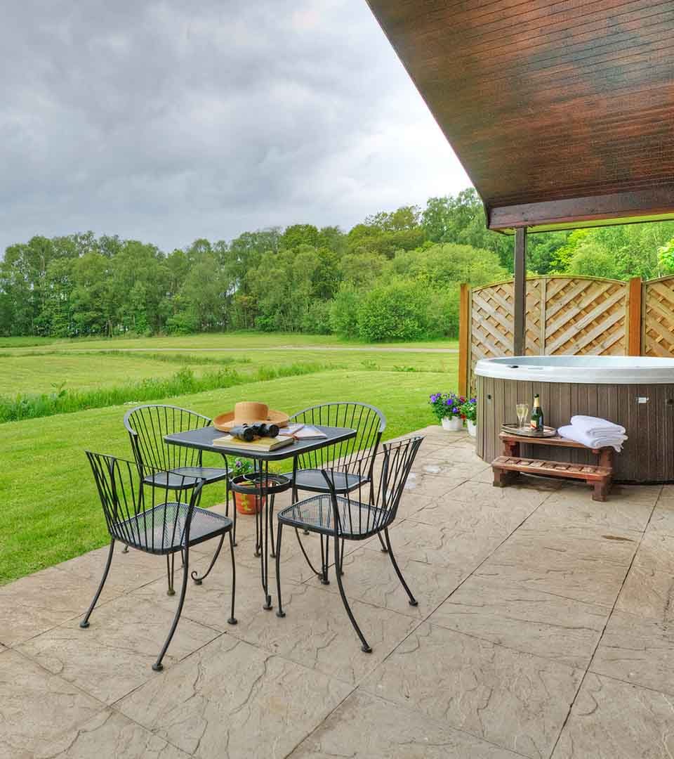 Outside patio with table, chairs and a hot tub with a view over Loch Lomond at a Chalet at Loch Lomond Waterfront