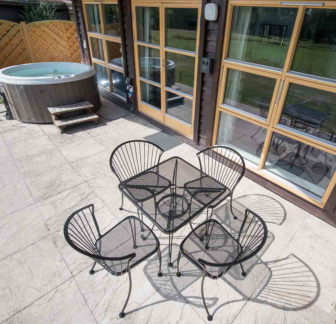 A patio outside a Chalet at Loch Lomond Waterfront with outside seating and hot tub on a sunny day