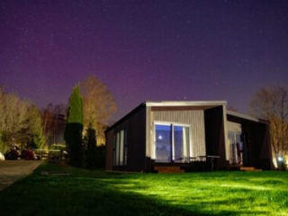 A Studio Lodge at night at Loch Lomond Waterfront with the Northern Lights in the sky.