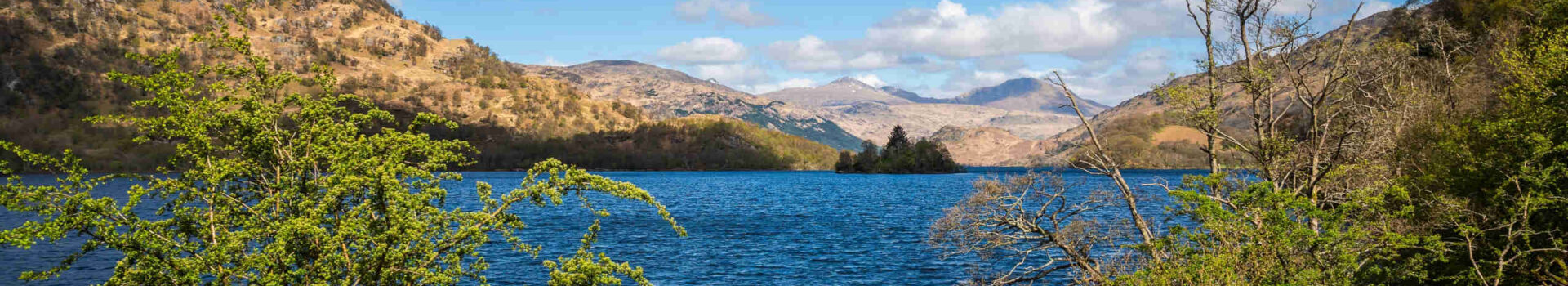 A serene view of Loch Lomond on a sunny day with a clear blue sky.