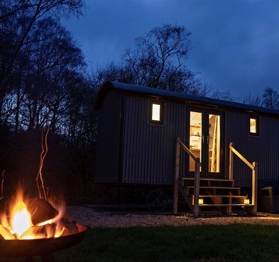 A Shepherd's Hut at Loch Lomond Waterfront on a winter's night with the fire pit lit outside