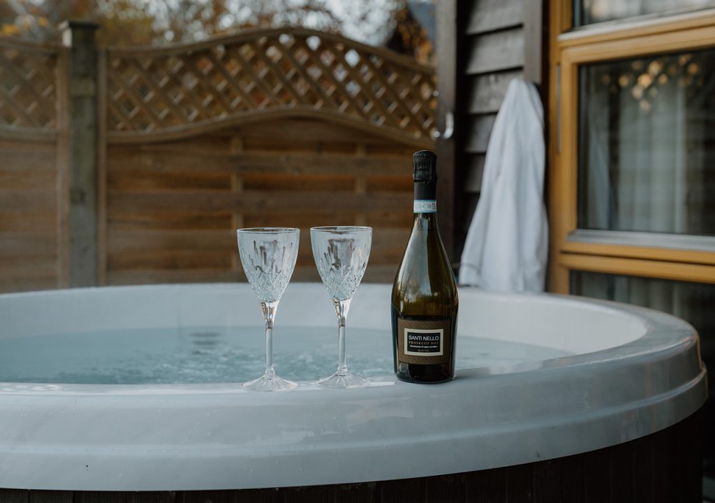 A chalets hot tub with two glasses and a bottle of champagne at Loch Lomond Waterfront