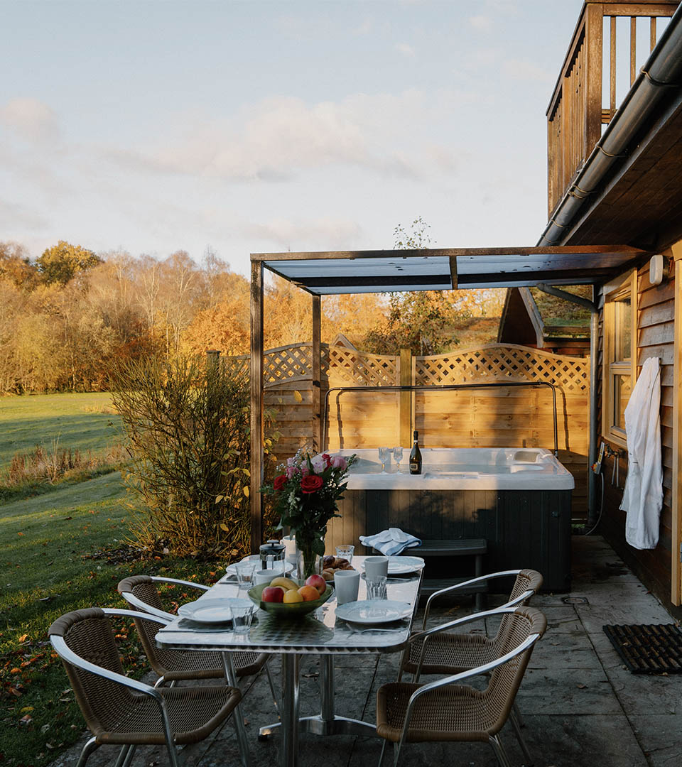 A romantic table set with flowers and robes by a bubbling hot tub at one of the luxury lodges at Loch Lomond Waterfront