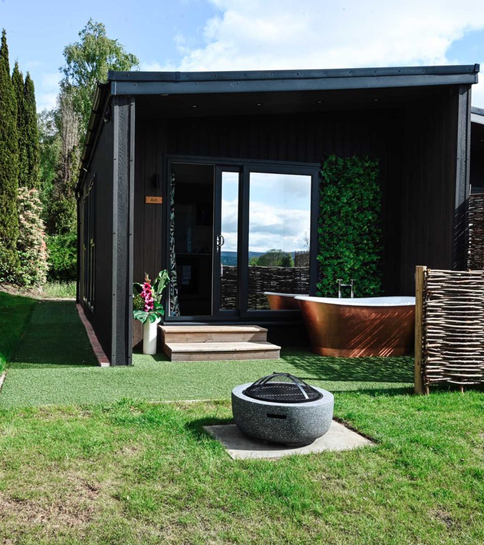 An outdoor copper bath, garden and firepit,outside Loch Lomonds Waterfront Cabins.
