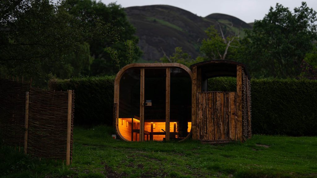 The exterior of the wild sauna at Loch Lomond Waterfont lit up in the evening.