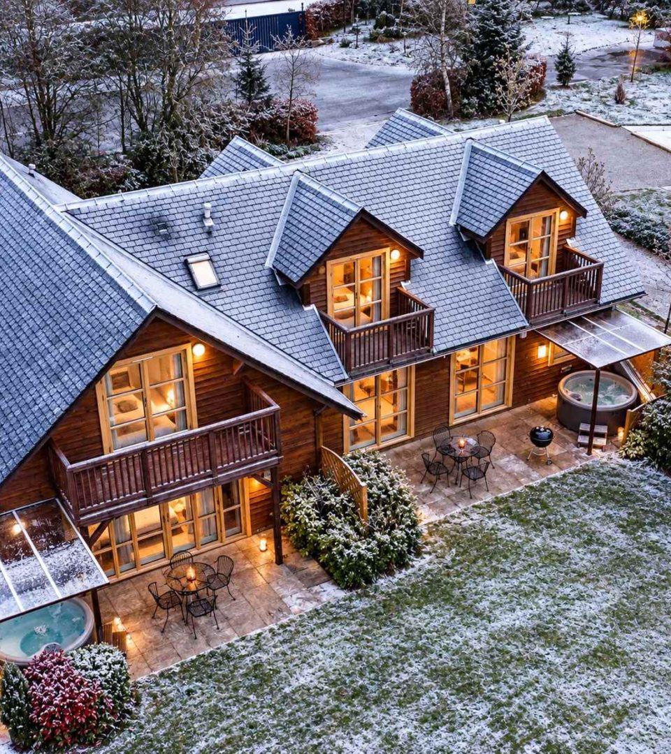 An overhead dron shot of Loch Lomond Waterfronts luxury lodges and hot tubs in winter with frost on the ground and cosy lights on inside.